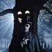 A man with dark glasses and a top hat, standing before a tree which has a face